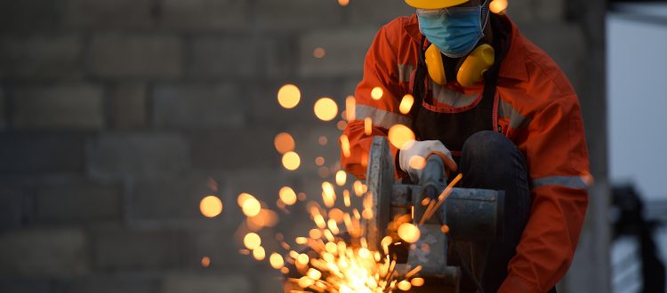 Metal worker grinding steel, wearing a safety helmet, mask and ear defenders